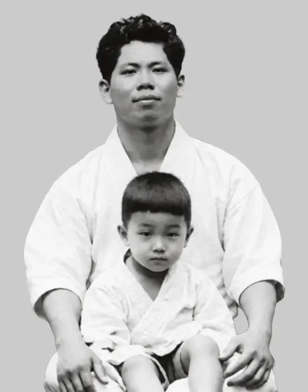 Master Yoshitaka Funakoshi seated in dogi holding a young child in dogi on his lap